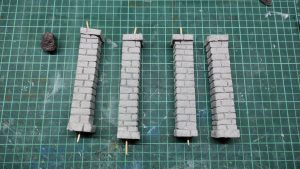 Diorama artesanal detallado de un duende y un pozo estructurado en tres niveles. El nivel superior recrea un jardín exterior exuberante utilizando vegetación natural y preservada (musgos y enredaderas), sobre estancias subterráneas de piedra y madera