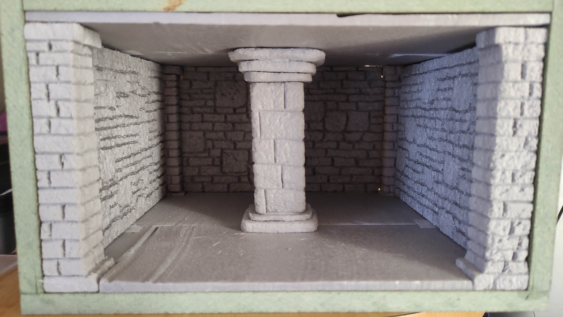 Diorama artesanal detallado de un duende y un pozo estructurado en tres niveles. El nivel superior recrea un jardín exterior exuberante utilizando vegetación natural y preservada (musgos y enredaderas), sobre estancias subterráneas de piedra y madera