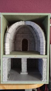 Diorama artesanal detallado de un duende y un pozo estructurado en tres niveles. El nivel superior recrea un jardín exterior exuberante utilizando vegetación natural y preservada (musgos y enredaderas), sobre estancias subterráneas de piedra y madera