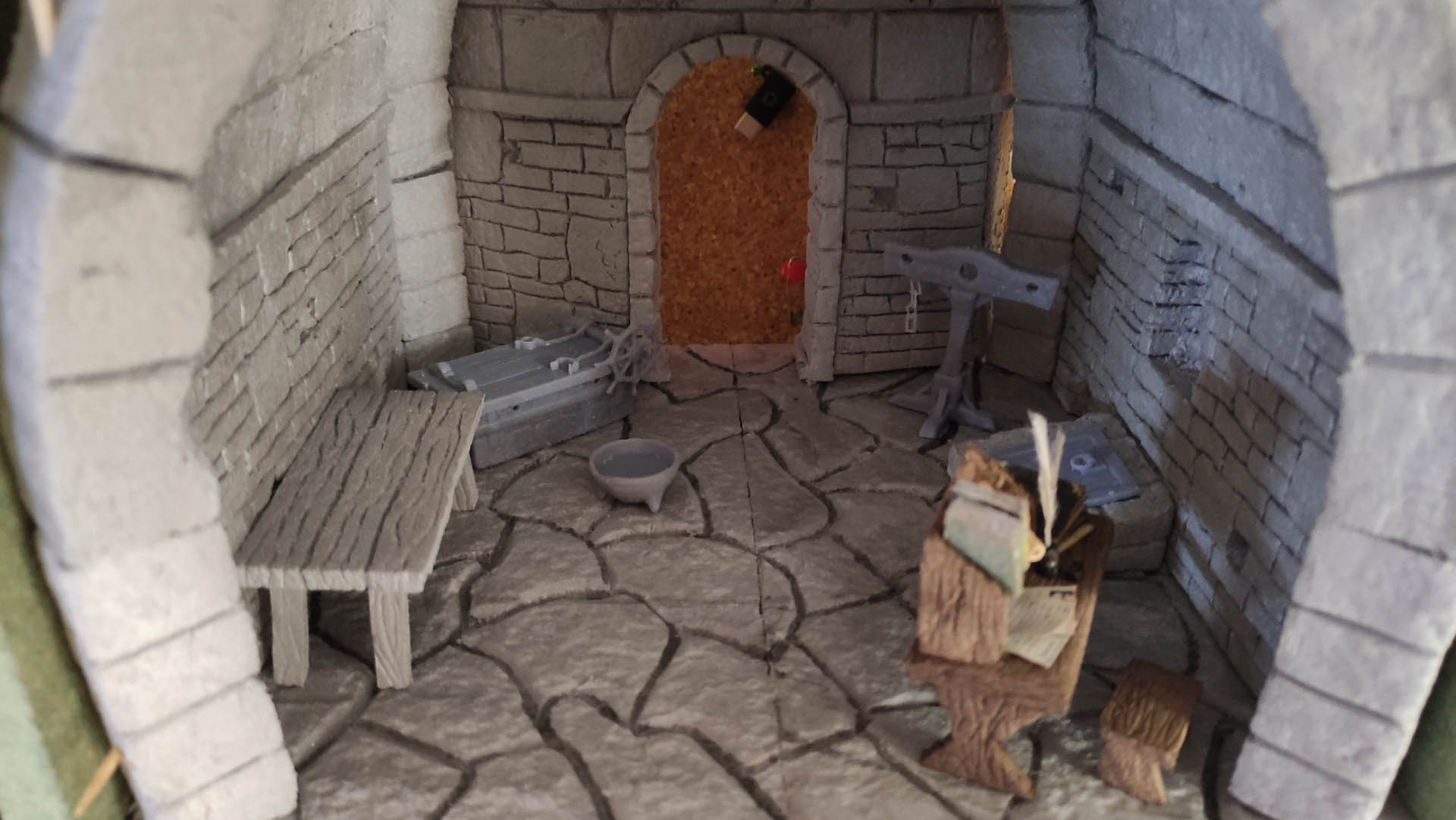 Diorama artesanal detallado de un duende y un pozo estructurado en tres niveles. El nivel superior recrea un jardín exterior exuberante utilizando vegetación natural y preservada (musgos y enredaderas), sobre estancias subterráneas de piedra y madera