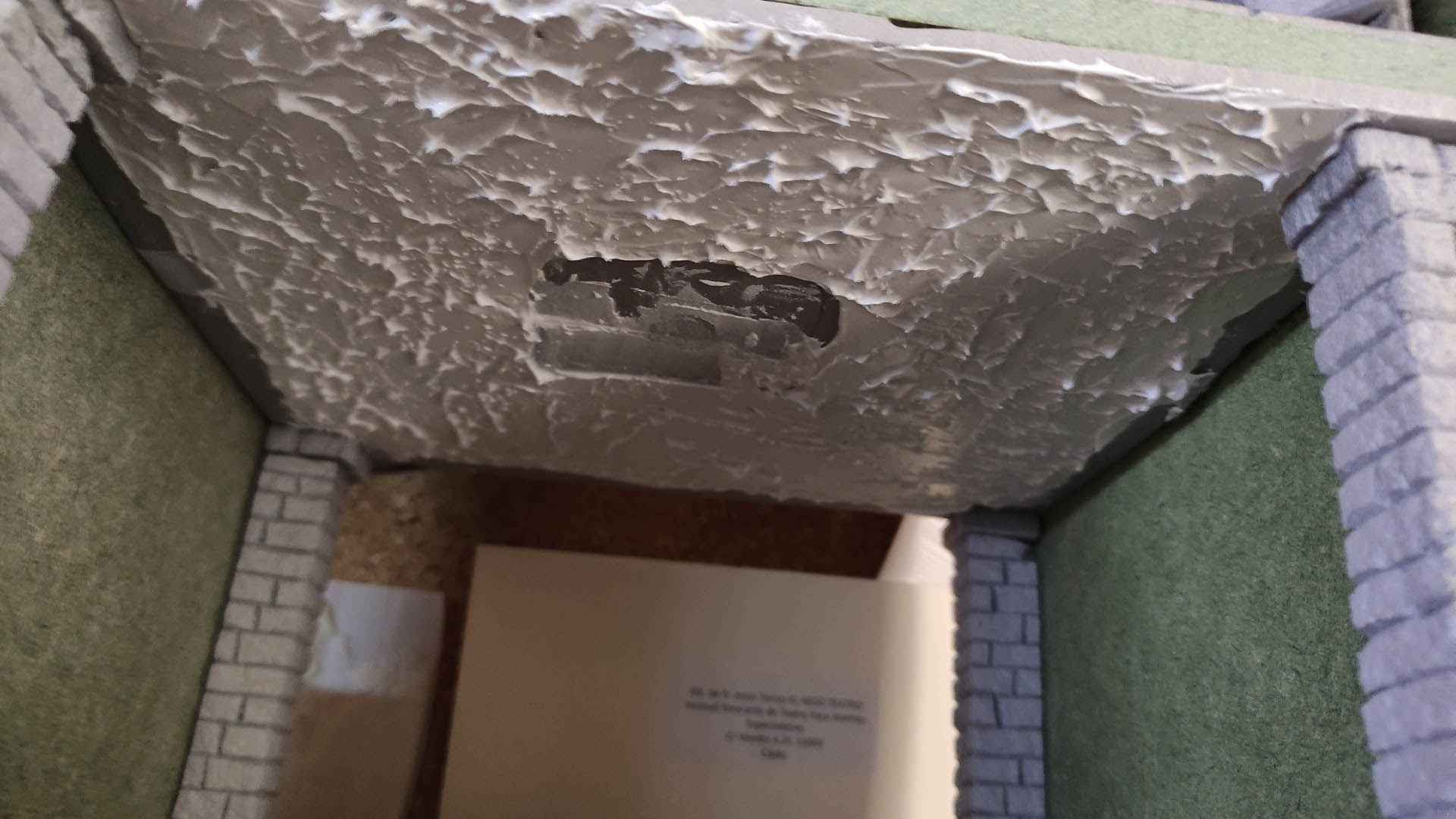 Diorama artesanal detallado de un duende y un pozo estructurado en tres niveles. El nivel superior recrea un jardín exterior exuberante utilizando vegetación natural y preservada (musgos y enredaderas), sobre estancias subterráneas de piedra y madera