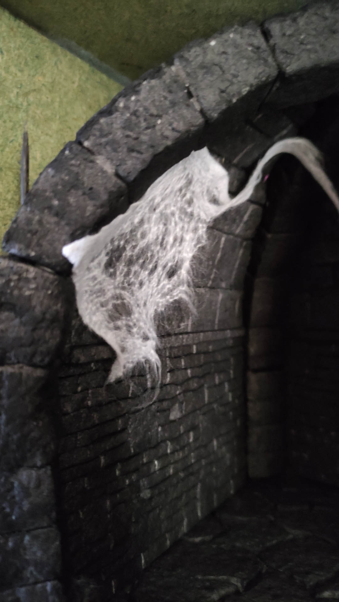 Diorama artesanal detallado de un duende y un pozo estructurado en tres niveles. El nivel superior recrea un jardín exterior exuberante utilizando vegetación natural y preservada (musgos y enredaderas), sobre estancias subterráneas de piedra y madera