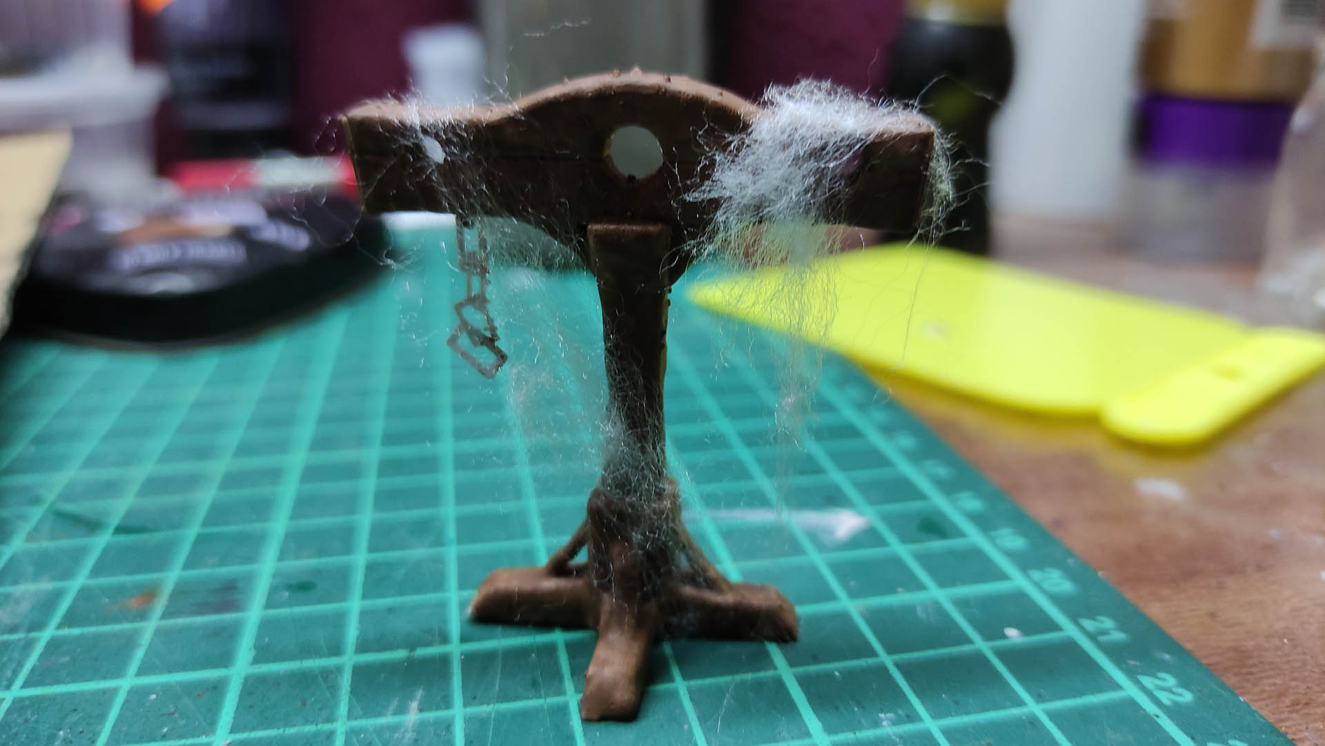 Diorama artesanal detallado de un duende y un pozo estructurado en tres niveles. El nivel superior recrea un jardín exterior exuberante utilizando vegetación natural y preservada (musgos y enredaderas), sobre estancias subterráneas de piedra y madera