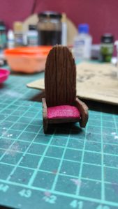 Diorama artesanal detallado de un duende y un pozo estructurado en tres niveles. El nivel superior recrea un jardín exterior exuberante utilizando vegetación natural y preservada (musgos y enredaderas), sobre estancias subterráneas de piedra y madera