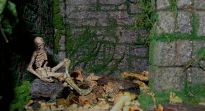 Diorama artesanal detallado de un duende y un pozo estructurado en tres niveles. El nivel superior recrea un jardín exterior exuberante utilizando vegetación natural y preservada (musgos y enredaderas), sobre estancias subterráneas de piedra y madera