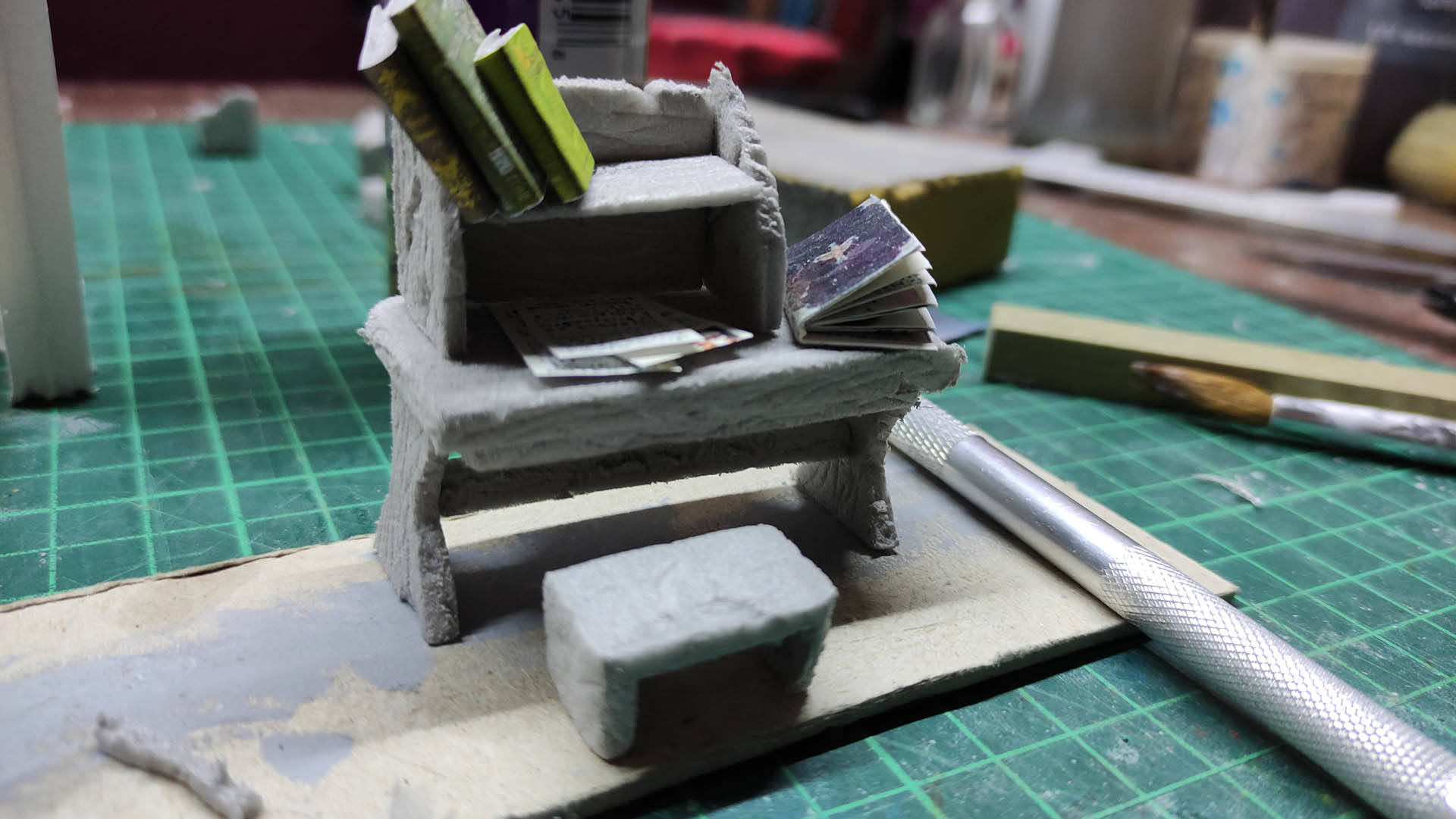 Diorama artesanal detallado de un duende y un pozo estructurado en tres niveles. El nivel superior recrea un jardín exterior exuberante utilizando vegetación natural y preservada (musgos y enredaderas), sobre estancias subterráneas de piedra y madera