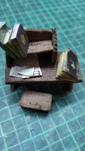 Diorama artesanal detallado de un duende y un pozo estructurado en tres niveles. El nivel superior recrea un jardín exterior exuberante utilizando vegetación natural y preservada (musgos y enredaderas), sobre estancias subterráneas de piedra y madera