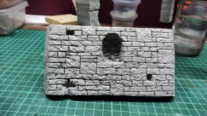 Diorama artesanal detallado de un duende y un pozo estructurado en tres niveles. El nivel superior recrea un jardín exterior exuberante utilizando vegetación natural y preservada (musgos y enredaderas), sobre estancias subterráneas de piedra y madera