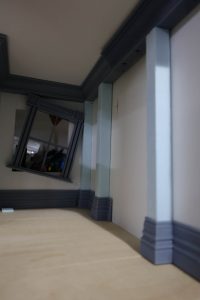 Proceso de construcción del diorama "Las Gemelas": recreación artesanal del pasillo del hotel Overlook con papel pintado geométrico en miniatura, carpintería detallada de puertas de hotel