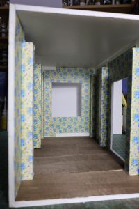 Proceso de construcción del diorama "Las Gemelas": recreación artesanal del pasillo del hotel Overlook con papel pintado geométrico en miniatura, carpintería detallada de puertas de hotel