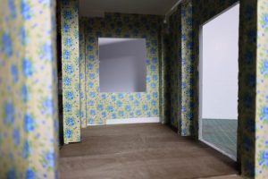 Proceso de construcción del diorama "Las Gemelas": recreación artesanal del pasillo del hotel Overlook con papel pintado geométrico en miniatura, carpintería detallada de puertas de hotel