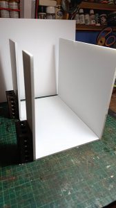 Proceso de construcción del diorama "Las Gemelas": recreación artesanal del pasillo del hotel Overlook con papel pintado geométrico en miniatura, carpintería detallada de puertas de hotel