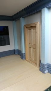 Proceso de construcción del diorama "Las Gemelas": recreación artesanal del pasillo del hotel Overlook con papel pintado geométrico en miniatura, carpintería detallada de puertas de hotel