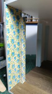 Proceso de construcción del diorama "Las Gemelas": recreación artesanal del pasillo del hotel Overlook con papel pintado geométrico en miniatura, carpintería detallada de puertas de hotel