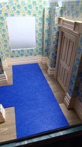 Proceso de construcción del diorama "Las Gemelas": recreación artesanal del pasillo del hotel Overlook con papel pintado geométrico en miniatura, carpintería detallada de puertas de hotel