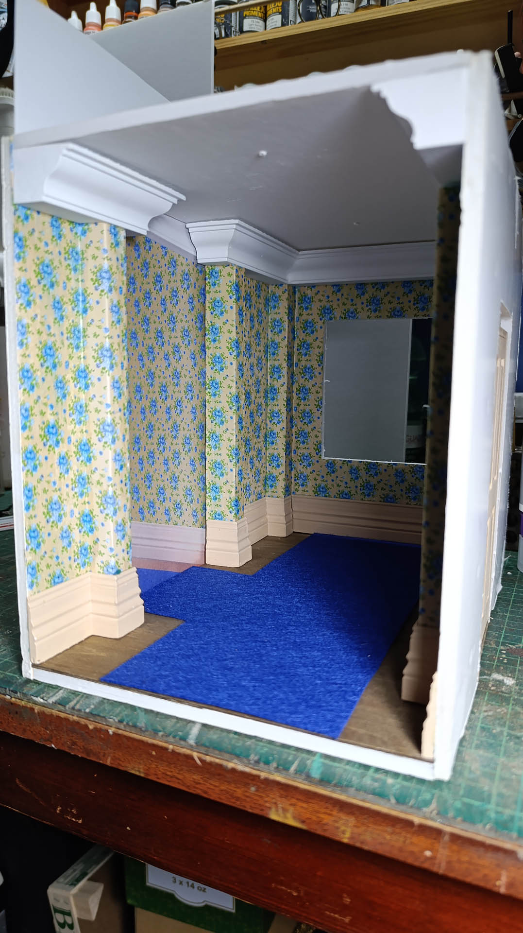 Proceso de construcción del diorama "Las Gemelas": recreación artesanal del pasillo del hotel Overlook con papel pintado geométrico en miniatura, carpintería detallada de puertas de hotel