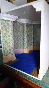 Proceso de construcción del diorama "Las Gemelas": recreación artesanal del pasillo del hotel Overlook con papel pintado geométrico en miniatura, carpintería detallada de puertas de hotel