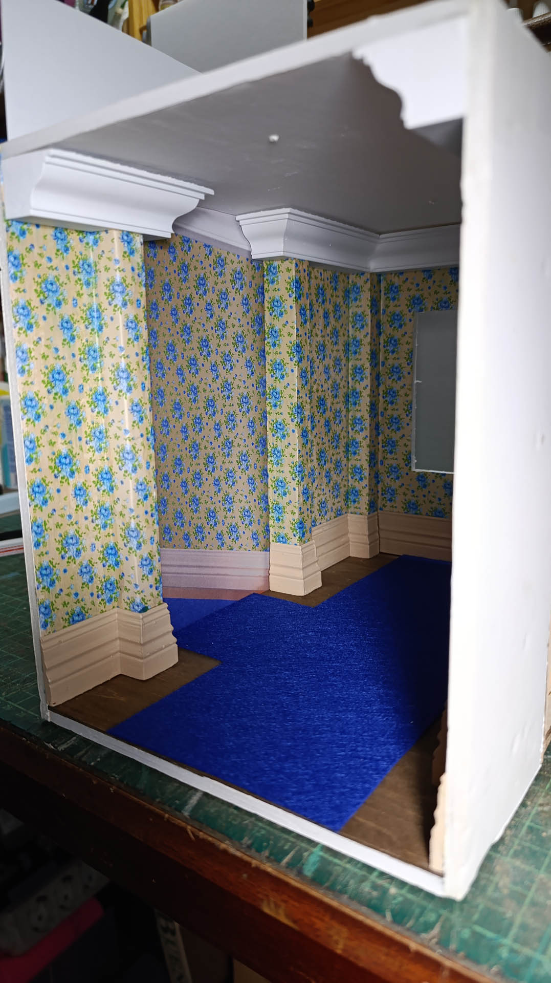 Proceso de construcción del diorama "Las Gemelas": recreación artesanal del pasillo del hotel Overlook con papel pintado geométrico en miniatura, carpintería detallada de puertas de hotel