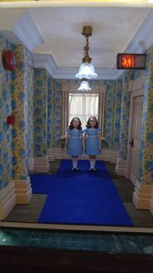 Proceso de construcción del diorama "Las Gemelas": recreación artesanal del pasillo del hotel Overlook con papel pintado geométrico en miniatura, carpintería detallada de puertas de hotel