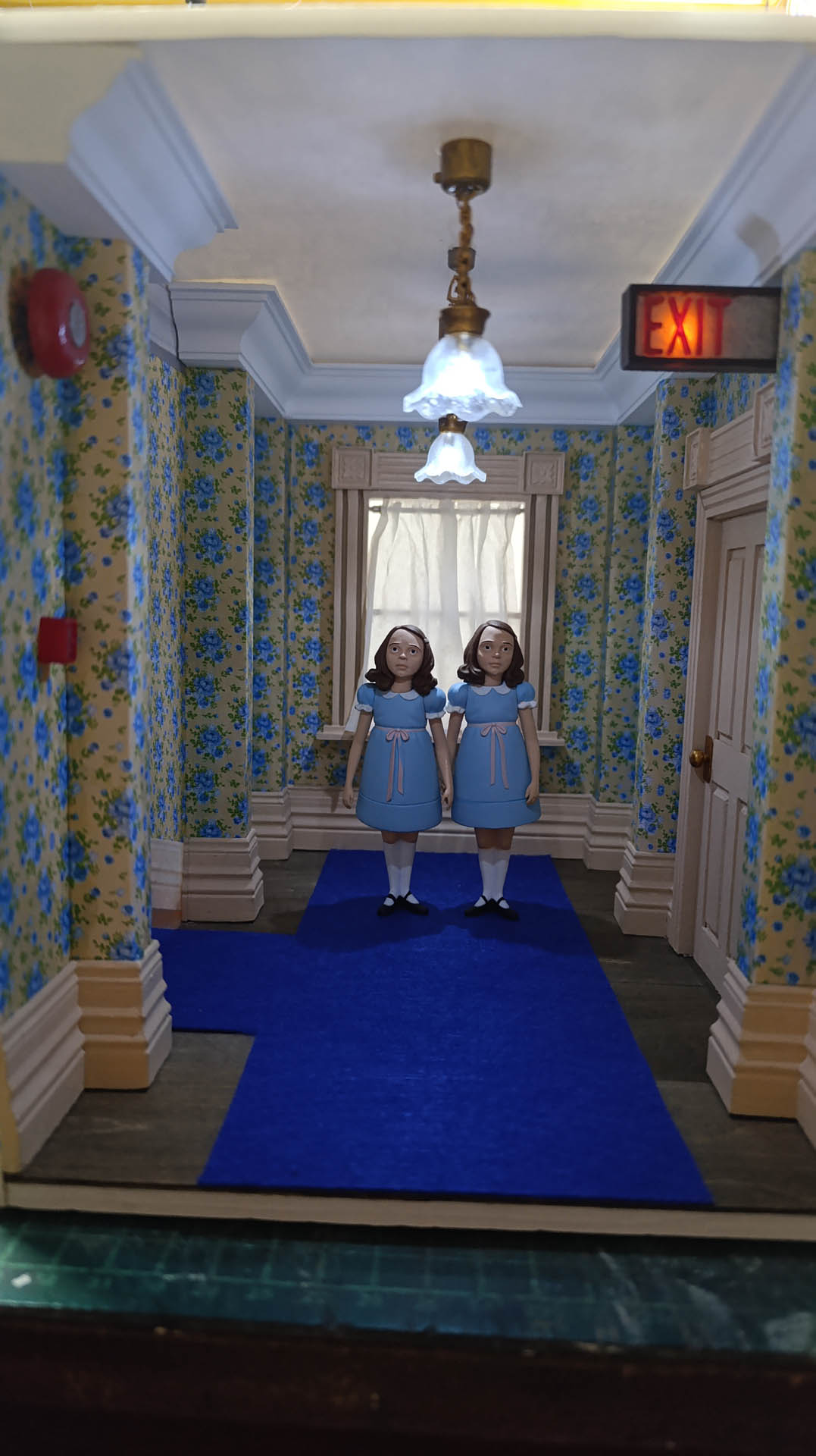 Proceso de construcción del diorama "Las Gemelas": recreación artesanal del pasillo del hotel Overlook con papel pintado geométrico en miniatura, carpintería detallada de puertas de hotel