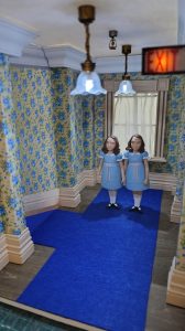 Proceso de construcción del diorama "Las Gemelas": recreación artesanal del pasillo del hotel Overlook con papel pintado geométrico en miniatura, carpintería detallada de puertas de hotel