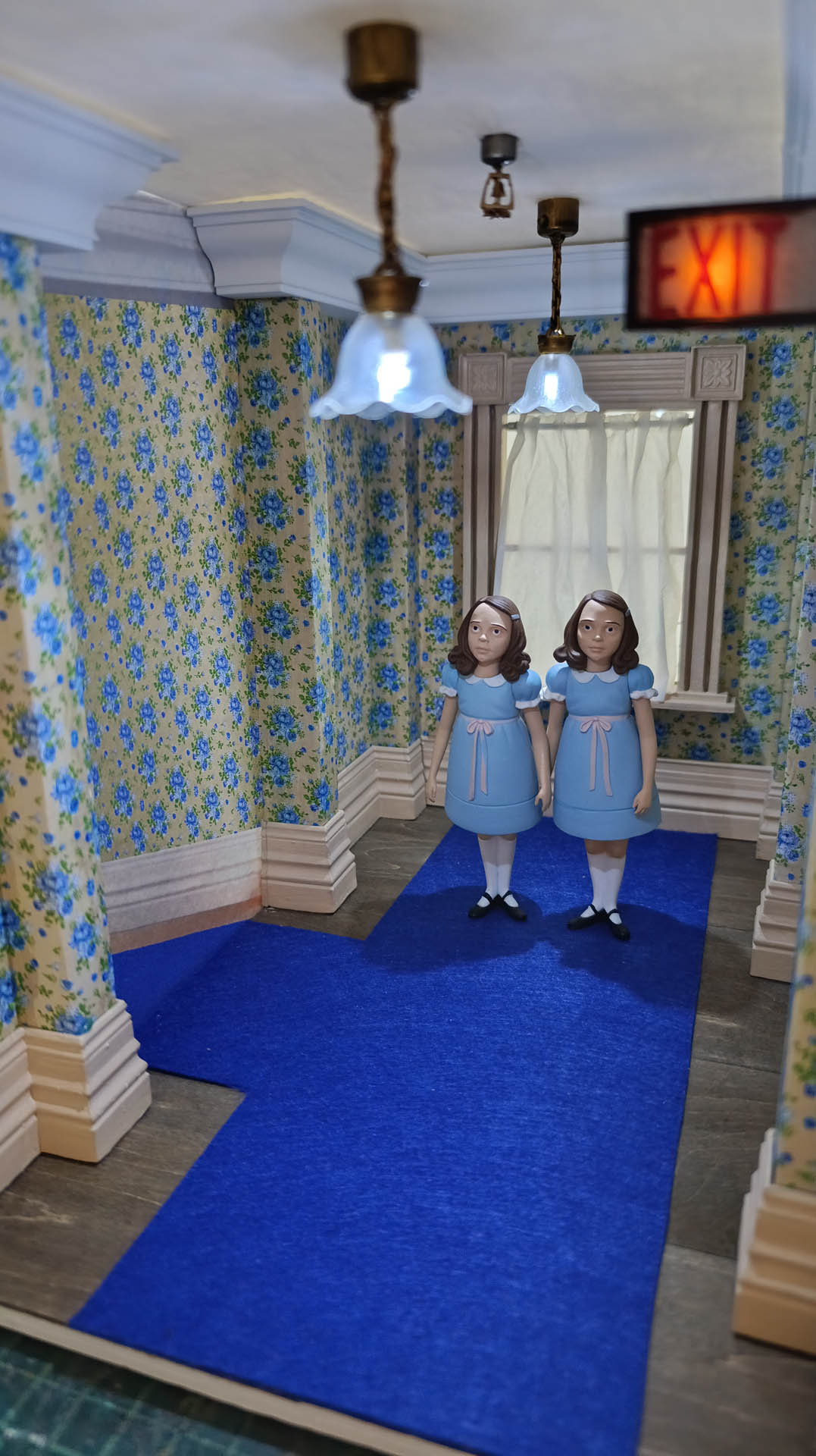 Proceso de construcción del diorama "Las Gemelas": recreación artesanal del pasillo del hotel Overlook con papel pintado geométrico en miniatura, carpintería detallada de puertas de hotel
