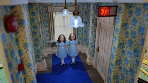 Proceso de construcción del diorama "Las Gemelas": recreación artesanal del pasillo del hotel Overlook con papel pintado geométrico en miniatura, carpintería detallada de puertas de hotel