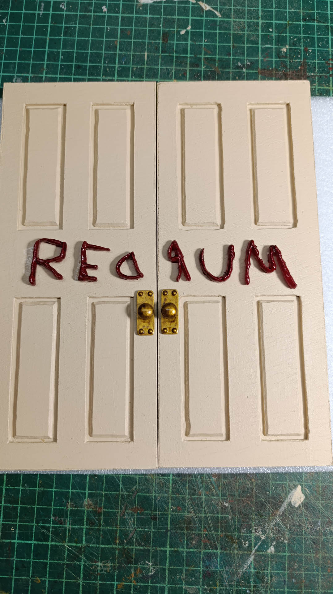 Proceso de construcción del diorama "Las Gemelas": recreación artesanal del pasillo del hotel Overlook con papel pintado geométrico en miniatura, carpintería detallada de puertas de hotel