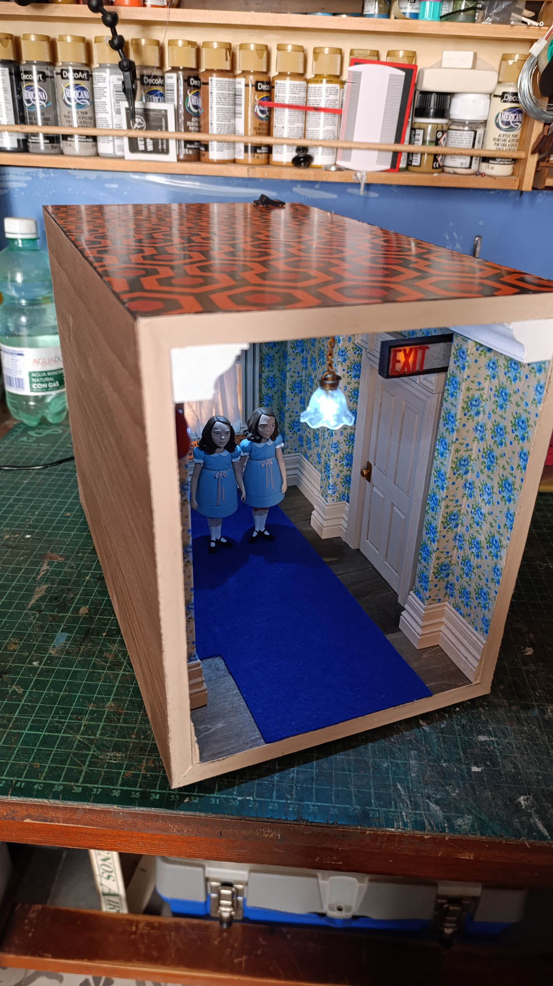 Proceso de construcción del diorama "Las Gemelas": recreación artesanal del pasillo del hotel Overlook con papel pintado geométrico en miniatura, carpintería detallada de puertas de hotel