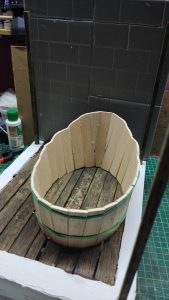 Proceso artesanal del diorama "El Nombre de la Rosa": recreación detallada de los baños del monasterio medieval con Berengario muerto en la bañera, modelado de texturas de piedra húmeda y envejecimiento de mobiliario de madera real