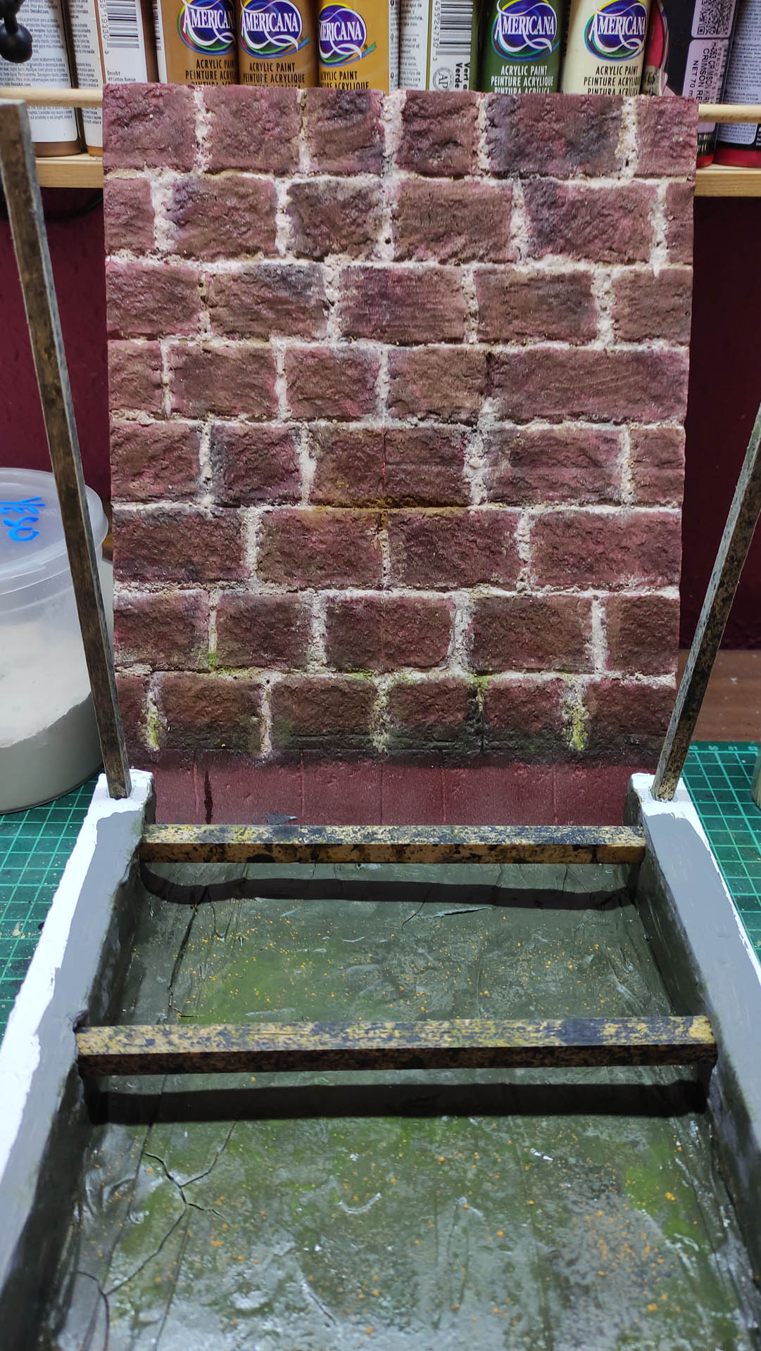 Proceso artesanal del diorama "El Nombre de la Rosa": recreación detallada de los baños del monasterio medieval con Berengario muerto en la bañera, modelado de texturas de piedra húmeda y envejecimiento de mobiliario de madera real