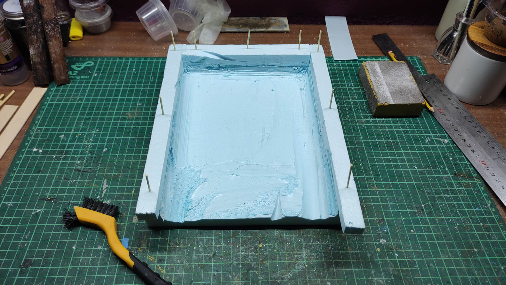 Proceso artesanal del diorama "El Nombre de la Rosa": recreación detallada de los baños del monasterio medieval con Berengario muerto en la bañera, modelado de texturas de piedra húmeda y envejecimiento de mobiliario de madera real