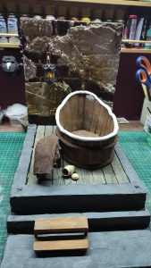 Proceso artesanal del diorama "El Nombre de la Rosa": recreación detallada de los baños del monasterio medieval con Berengario muerto en la bañera, modelado de texturas de piedra húmeda y envejecimiento de mobiliario de madera real