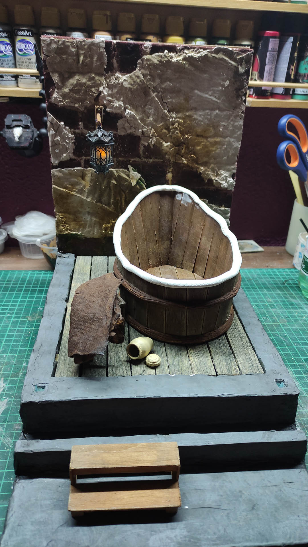 Proceso artesanal del diorama "El Nombre de la Rosa": recreación detallada de los baños del monasterio medieval con Berengario muerto en la bañera, modelado de texturas de piedra húmeda y envejecimiento de mobiliario de madera real