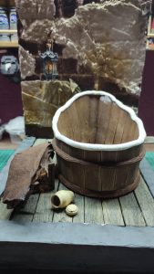 Proceso artesanal del diorama "El Nombre de la Rosa": recreación detallada de los baños del monasterio medieval con Berengario muerto en la bañera, modelado de texturas de piedra húmeda y envejecimiento de mobiliario de madera real