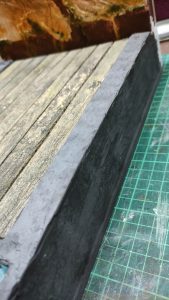 Proceso artesanal del diorama "El Nombre de la Rosa": recreación detallada de los baños del monasterio medieval con Berengario muerto en la bañera, modelado de texturas de piedra húmeda y envejecimiento de mobiliario de madera real