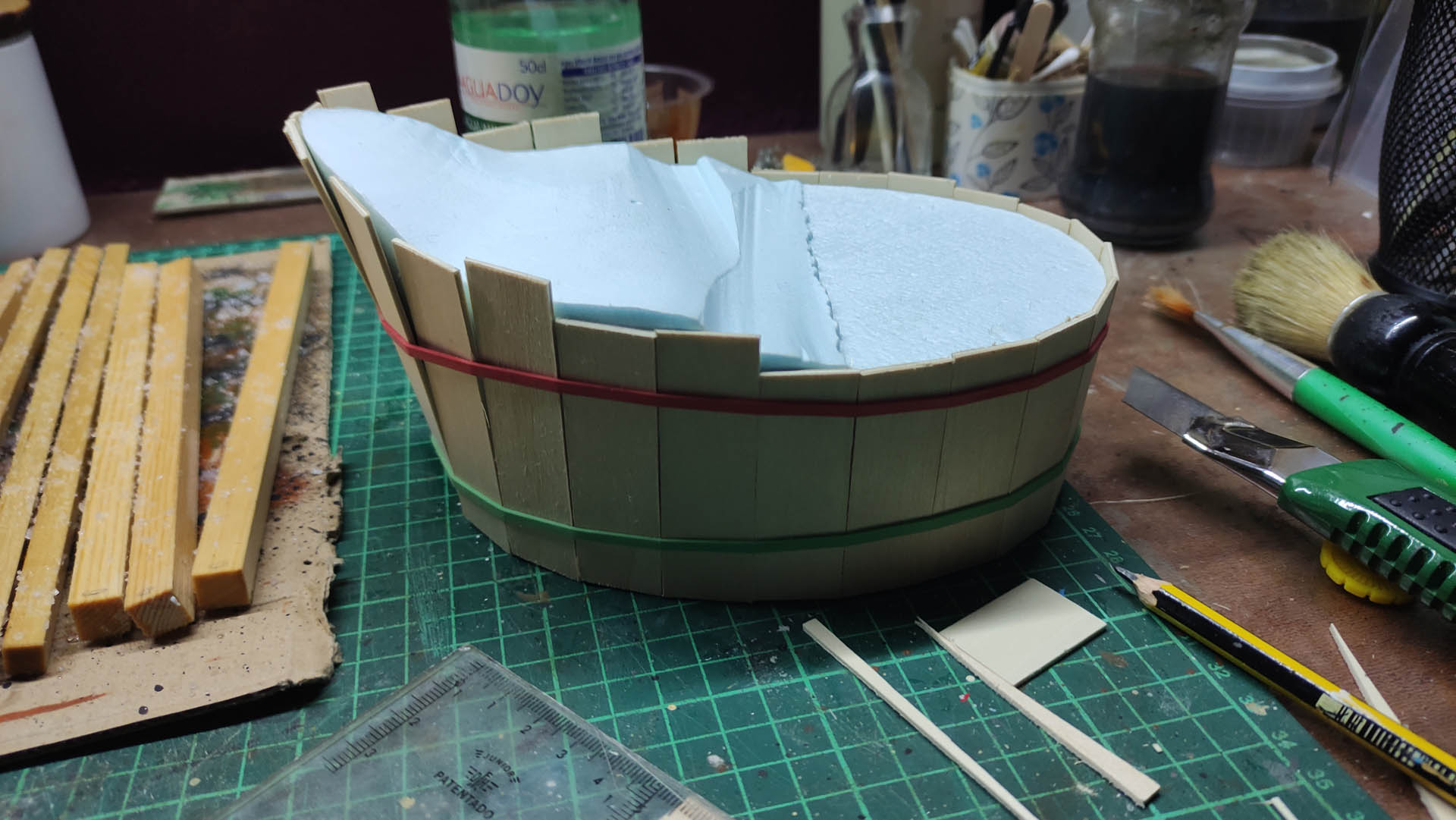 Proceso artesanal del diorama "El Nombre de la Rosa": recreación detallada de los baños del monasterio medieval con Berengario muerto en la bañera, modelado de texturas de piedra húmeda y envejecimiento de mobiliario de madera real