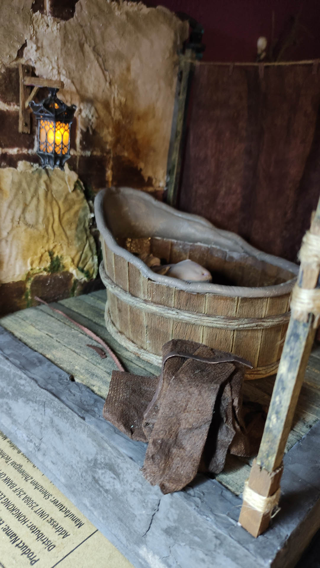 Proceso artesanal del diorama "El Nombre de la Rosa": recreación detallada de los baños del monasterio medieval con Berengario muerto en la bañera, modelado de texturas de piedra húmeda y envejecimiento de mobiliario de madera real