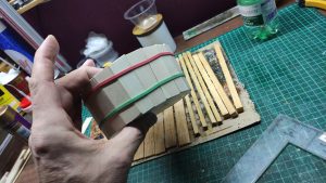 Proceso artesanal del diorama "El Nombre de la Rosa": recreación detallada de los baños del monasterio medieval con Berengario muerto en la bañera, modelado de texturas de piedra húmeda y envejecimiento de mobiliario de madera real