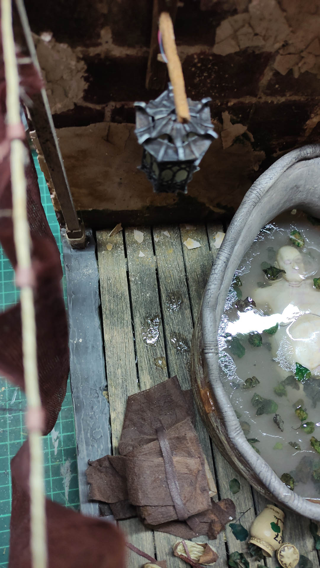 Proceso artesanal del diorama "El Nombre de la Rosa": recreación detallada de los baños del monasterio medieval con Berengario muerto en la bañera, modelado de texturas de piedra húmeda y envejecimiento de mobiliario de madera real