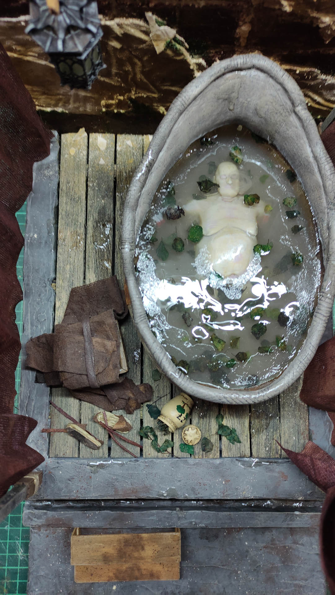 Proceso artesanal del diorama "El Nombre de la Rosa": recreación detallada de los baños del monasterio medieval con Berengario muerto en la bañera, modelado de texturas de piedra húmeda y envejecimiento de mobiliario de madera real