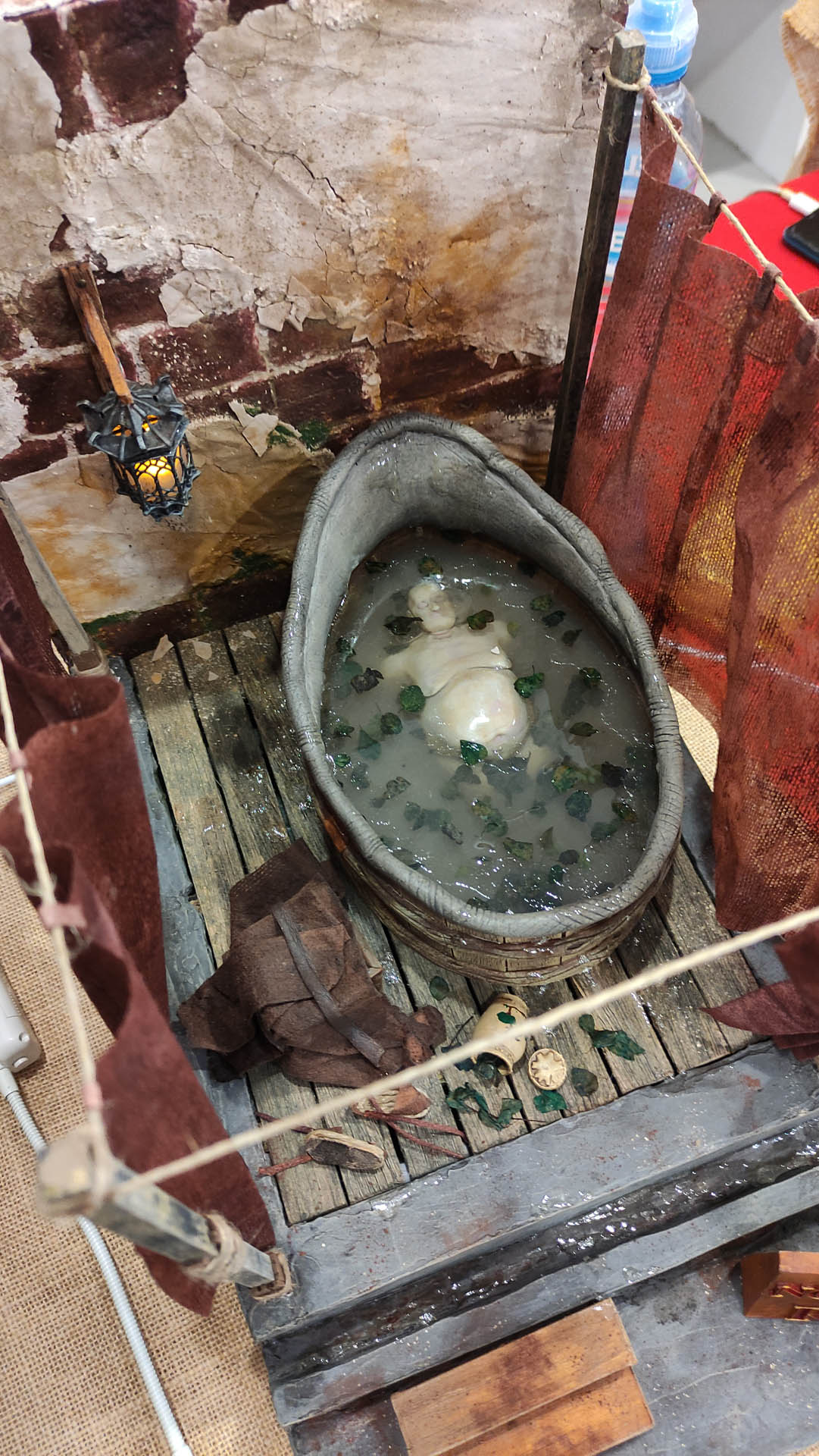 Proceso artesanal del diorama "El Nombre de la Rosa": recreación detallada de los baños del monasterio medieval con Berengario muerto en la bañera, modelado de texturas de piedra húmeda y envejecimiento de mobiliario de madera real