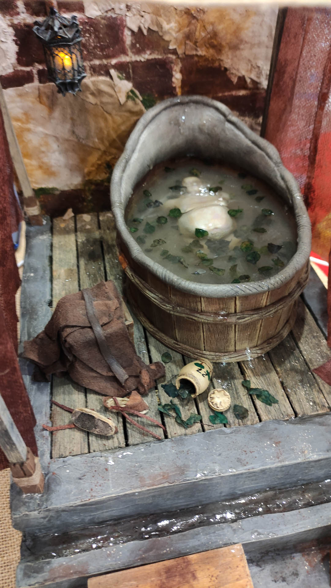 Proceso artesanal del diorama "El Nombre de la Rosa": recreación detallada de los baños del monasterio medieval con Berengario muerto en la bañera, modelado de texturas de piedra húmeda y envejecimiento de mobiliario de madera real