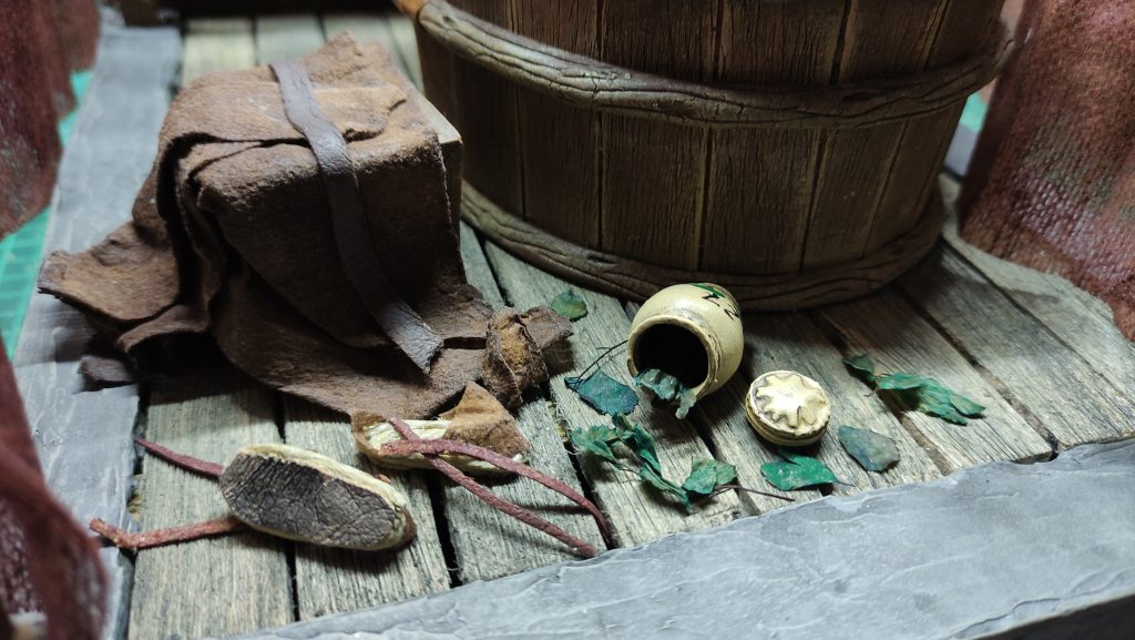 Proceso artesanal del diorama "El Nombre de la Rosa": recreación detallada de los baños del monasterio medieval con Berengario muerto en la bañera, modelado de texturas de piedra húmeda y envejecimiento de mobiliario de madera real
