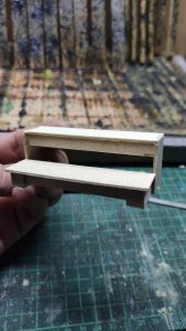 Proceso artesanal del diorama "El Nombre de la Rosa": recreación detallada de los baños del monasterio medieval con Berengario muerto en la bañera, modelado de texturas de piedra húmeda y envejecimiento de mobiliario de madera real