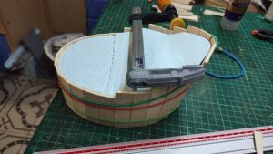 Proceso artesanal del diorama "El Nombre de la Rosa": recreación detallada de los baños del monasterio medieval con Berengario muerto en la bañera, modelado de texturas de piedra húmeda y envejecimiento de mobiliario de madera real