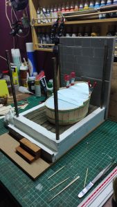 Proceso artesanal del diorama "El Nombre de la Rosa": recreación detallada de los baños del monasterio medieval con Berengario muerto en la bañera, modelado de texturas de piedra húmeda y envejecimiento de mobiliario de madera real