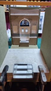 Diorama artesanal de Venecia durante la peste negra, mostrando a dos médicos de la peste con máscara frente a una góndola en un canal, con iluminación de farol.