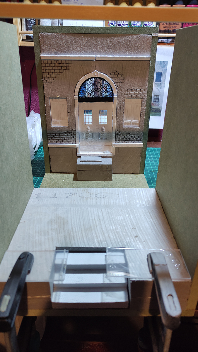 Diorama artesanal de Venecia durante la peste negra, mostrando a dos médicos de la peste con máscara frente a una góndola en un canal, con iluminación de farol.