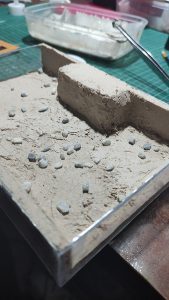 Diorama artesanal de Venecia durante la peste negra, mostrando a dos médicos de la peste con máscara frente a una góndola en un canal, con iluminación de farol.